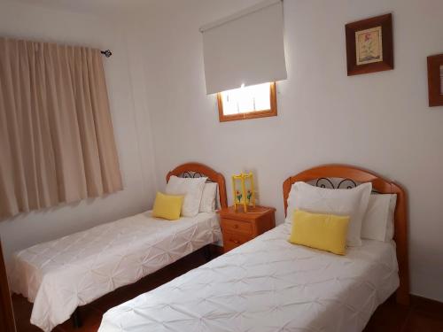 two beds in a room with white sheets and yellow pillows at Vv - Casa Clary -Finca Medina in Alojera
