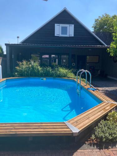 a swimming pool with a wooden deck and a house at La Casa Gardenia in Drunen