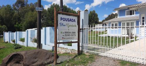 a white fence with a sign in front of a house at POUSADA BLUE GARDEN in Lages