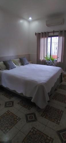 1 dormitorio con 1 cama blanca grande y ventana en Viví Iguazú Casa Familiar en Puerto Iguazú