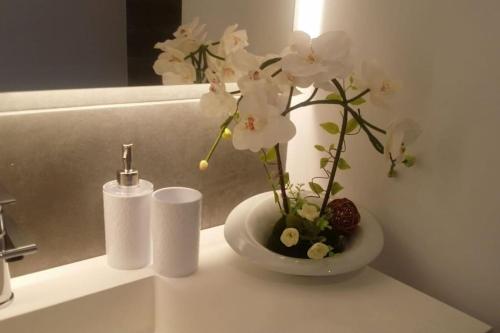 un vaso bianco con fiori bianchi sul bancone del bagno di VILLA NOKA a Cala en Blanes