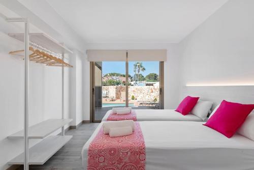 una camera bianca con un grande letto con cuscini rosa di VILLA NOKA a Cala en Blanes
