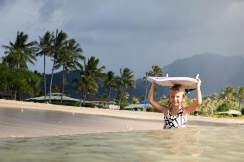 a girl in the water with a surfboard on her head at The Cliffs at Princeville in Princeville