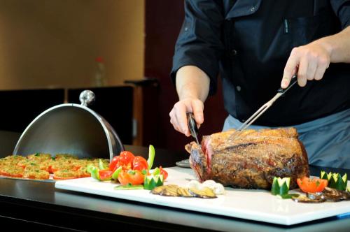 a person cutting a piece of meat with tongs at Campanile Prime Paris 19 - La Villette in Paris