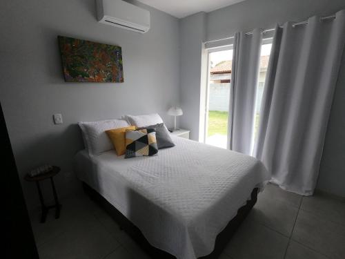 a bedroom with a bed with white sheets and a window at Rosa Surf Hostel & Food in Praia do Rosa