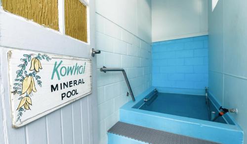 a bathroom with a blue tub and a sign on the wall at Kowhai Motel Rotorua in Rotorua