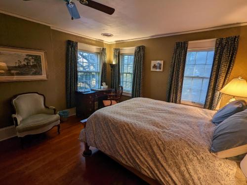 a bedroom with a bed and a chair and windows at English Cottage in Greensboro