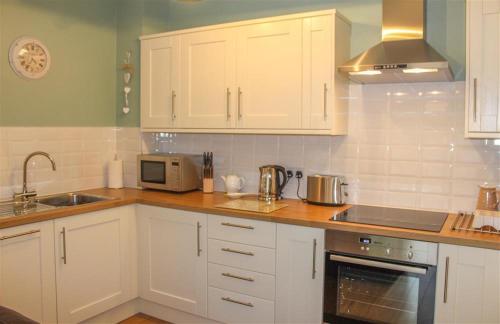 een keuken met witte kasten, een wastafel en een magnetron bij Four Seasons Cottage in Ambleside