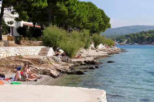 a group of people sitting on the beach near the water at Holiday house with a parking space Milna, Brac - 20140 in Milna