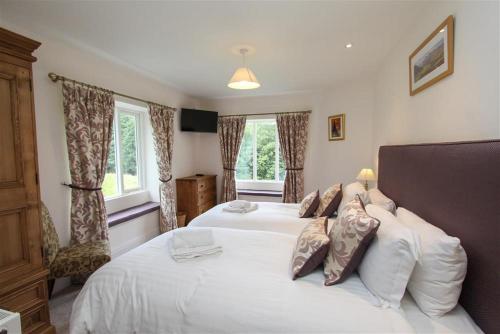 a bedroom with two white beds and two windows at Elterwater Lodge in Little Langdale