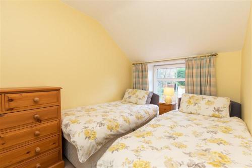 a bedroom with two beds and a dresser and a window at Millcroft Cottage in Penrith