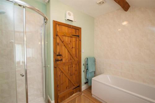 a bathroom with a shower and a tub and a wooden door at Grisedale Cottage in Keswick