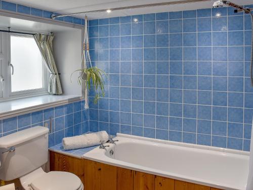 a blue tiled bathroom with a tub and a toilet at The Old Butchers Shop in Wereham