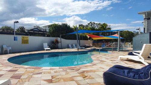 a swimming pool with chairs and umbrellas on a patio at Alex Beach Cabins and Tourist Park in Alexandra Headland