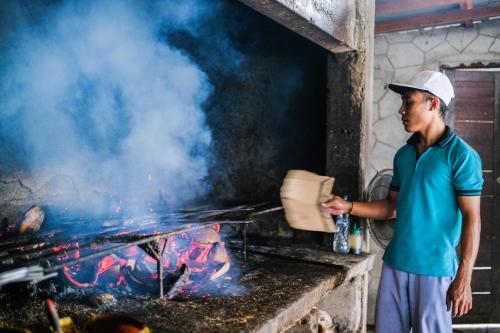 a man is cooking food on a grill at RedDoorz at Tanjung Alam Hotel Lovina in Buleleng