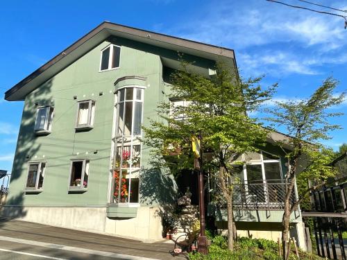 una casa verde con un árbol delante en Pension Puutaro en Zao Onsen