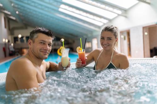 a man and woman in a swimming pool with drinks at Ski & Wellness Residence Družba in Demanovska Dolina