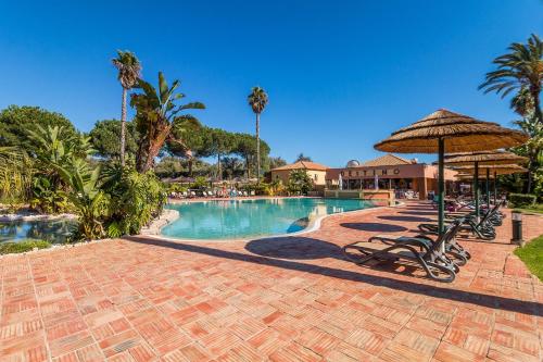 a swimming pool with chairs and an umbrella at Jardins Meia Praia 104 by Algarve Golden Properties in Lagos