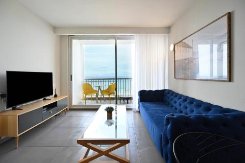 ein Wohnzimmer mit einem blauen Sofa und einem TV in der Unterkunft Life`s A Beach by HolyGuest in Tel Aviv