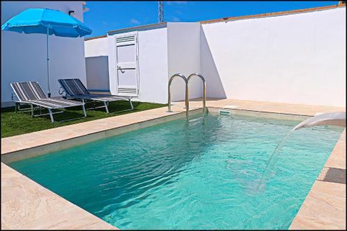 una piscina con due sedie e un ombrellone di Chalet los Morenos a Conil de la Frontera