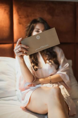a woman sitting on a bed holding a book at Bajka Hotel & Resort in Grodziec