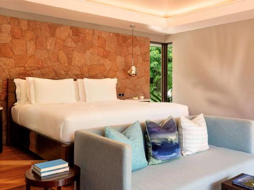 a bedroom with a large bed and a couch with pillows at Raffles Seychelles in Baie Sainte Anne