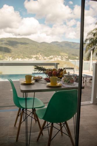 a table with a bowl of fruit and two green chairs at Paraíso da Enseada de Brito in Palhoça