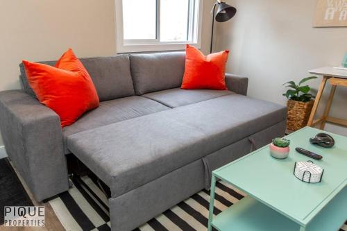 a living room with a gray couch with orange pillows at NEW, Euro-Style Suite, Whyte Avenue, AC, Netflix, Sleeps 6! in Edmonton