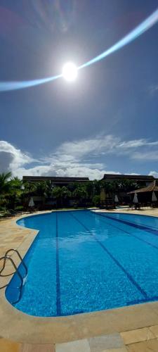 a large blue swimming pool with the sun in the sky at Apartamento em guarajuba 200m da praia in Camaçari