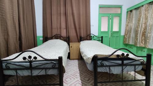 zwei Betten in einem Zimmer mit grünen Wänden und Vorhängen in der Unterkunft Issa's House in Bayt Sāḩūr