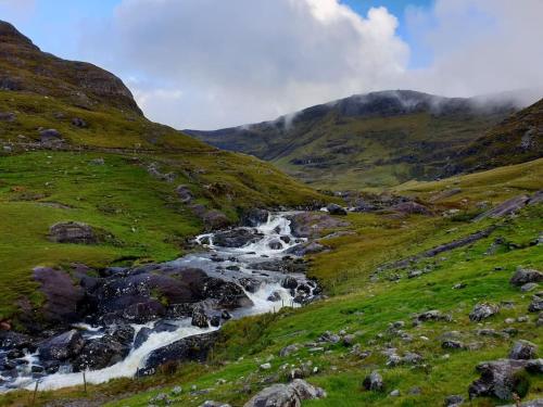 a river in the middle of a grassy hill at Secluded cottage nestled in the Beara Peninsula in Killarney