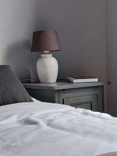 a bed with a table with a lamp and a book at La Petite Histoire gîtes-appartements in Ath