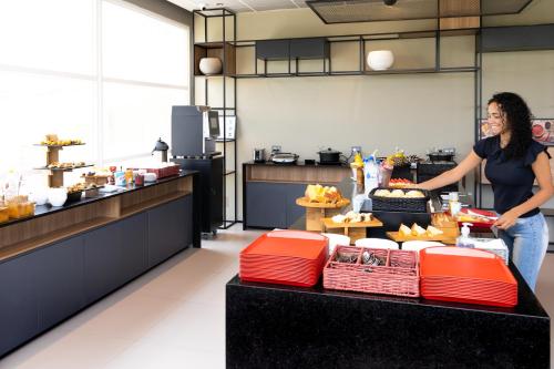 a woman standing behind a counter in a kitchen at Ibis Aruja in Arujá