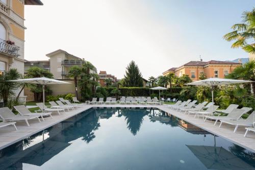 una piscina con sedie bianche e ombrelloni di Grand Hotel Liberty a Riva del Garda