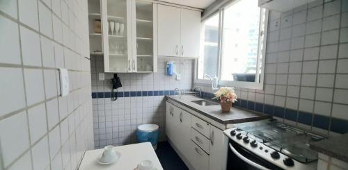 eine weiß geflieste Küche mit einem Waschbecken und einem Fenster in der Unterkunft Apartamento Aconchego na Praia da Costa in Vila Velha
