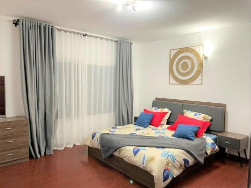 - une chambre avec un lit doté d'oreillers bleus et rouges dans l'établissement Appartements - Le Paradisier Ambatobe, à Antananarivo