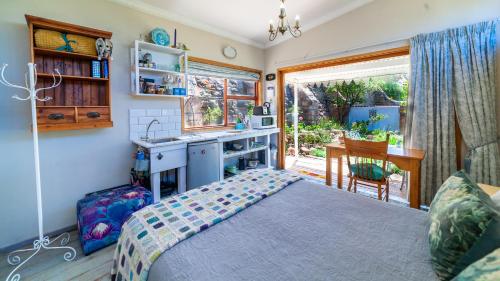 a bedroom with a bed and a kitchen with a window at The Amberley Annex in Muizenberg