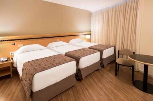 a hotel room with three beds and a table at Hotel Golden Park Internacional Foz & Convenções By Nacional Inn in Foz do Iguaçu