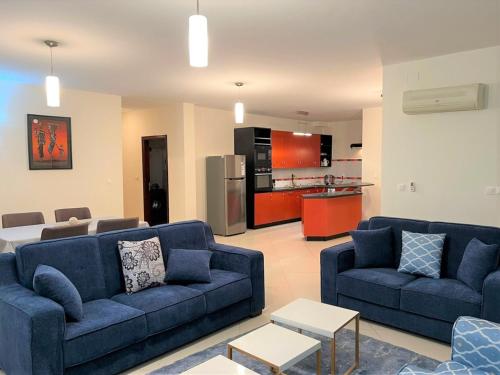 a living room with two blue couches and a kitchen at Appartements - Le Paradisier Ambatobe in Antananarivo