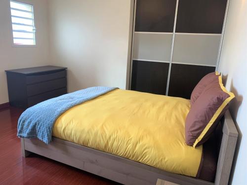 a bed with a yellow blanket and a night stand at Appartements - Le Paradisier Ambatobe in Antananarivo