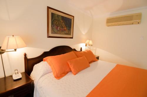 a bedroom with a bed with orange pillows and a phone at Hotel Majestic in Barranquilla
