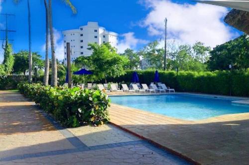 a swimming pool with chairs and a building in the background at Juan Dolio-2da Línea de Playa-Acceso Privado-Piscina-Área de Bbq-Gazebos-Jardines-Balcones-Wifi-Telecable-Netflix-Disney Plus-Campos de Gof-Excursiones-Plazas Comerciales-Minimarket-Restaurantes-Bares-Clubes de Playa in Guayacanes