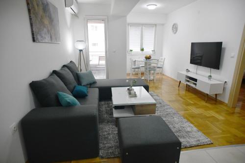 ein Wohnzimmer mit einem schwarzen Sofa und einem Tisch in der Unterkunft Modern & Cozy near City Center with Balcony, free Parking and coffee in Skopje