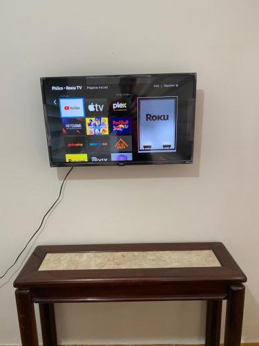 a tv on a wall with a wooden table at Casa aconchegante à 400m da Praia da Tartaruga - Ar condicionado - WIFI 450MB - Netflix - Cozinha Completa - Garagem in Rio das Ostras
