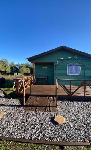 a green building with a wooden deck and a house at Cabañas Vista Hermosa Radal 7 Tazas in El Torreón