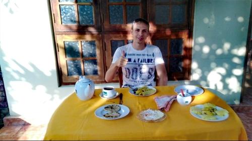 a man sitting at a yellow table with food at ARANI HOMESTAY in Polonnaruwa