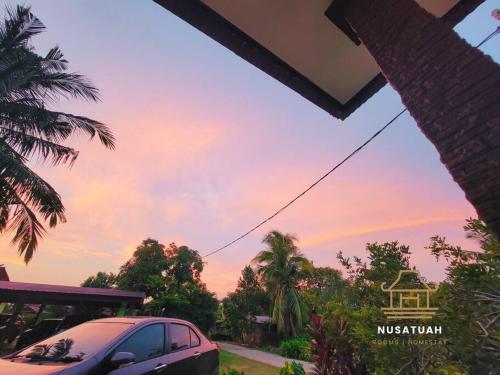 a car parked in front of a house with a sunset at NusaTuah Roomstay in Melaka