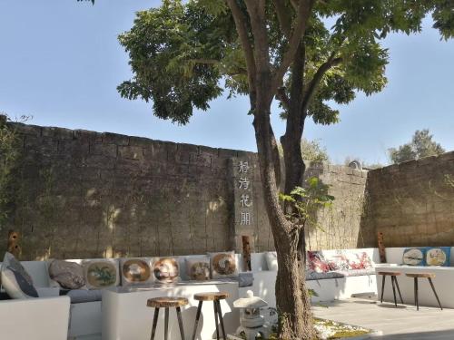 a tree in front of a wall with couches and tables at Waiting for the Blossoms B&B Tea House in Shantou