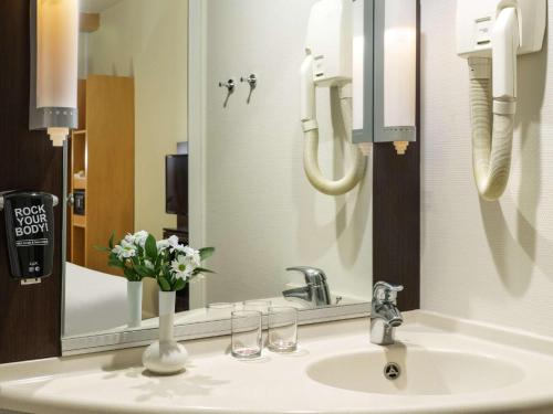 a bathroom sink with a mirror and a vase of flowers at Ibis Kayseri in Kayseri
