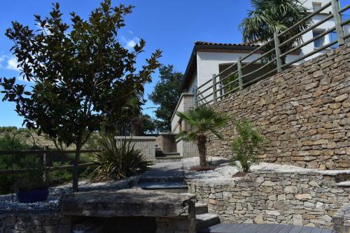 a house with a stone wall and trees in front of it at Chambre au calme avec spa privatif gratuit sud aveyron les palmiers des causses in Saint-Rome-de-Tarn
